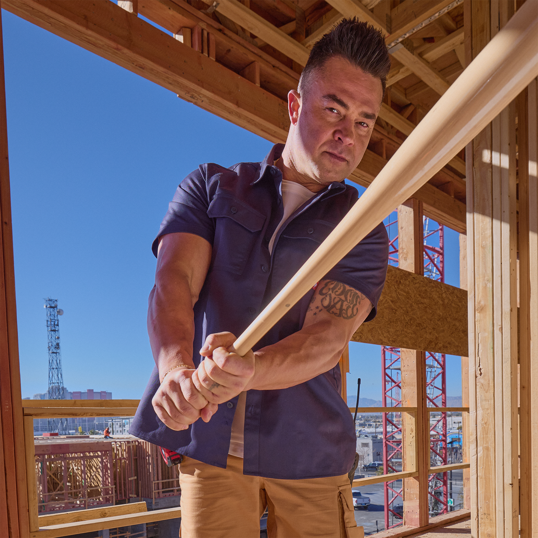 Nick Swisher holding a baseball bat inside a wooden framed building under construction.