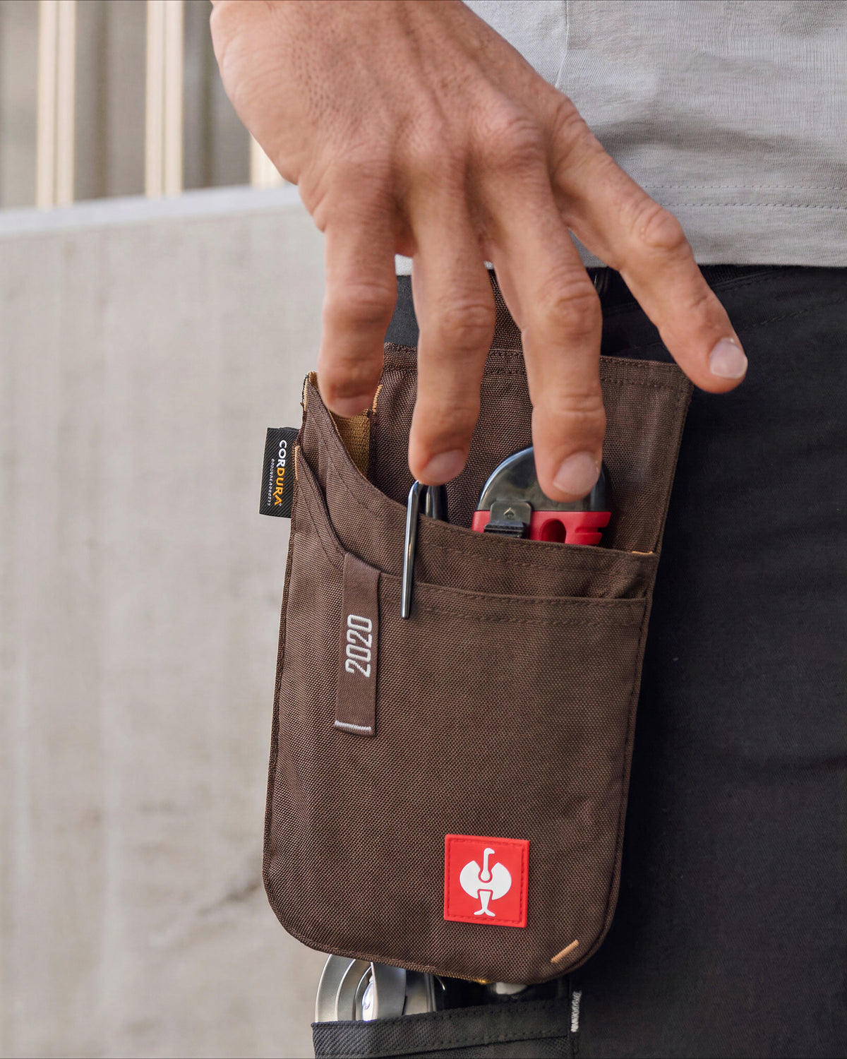 Small chestnut STRAUSS e.s.motion 2020 tool bag worn at the hip, holding pliers as a hand reaches inside.