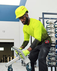 A bright yellow STRAUSS Baseball Style Hard Hat with a visor on a model working in a wheel factory, seen from the front.