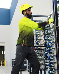 A bright yellow STRAUSS Baseball Style Hard Hat with a visor on a model working in a wheel factory.