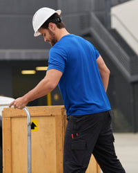 A worker wears the STRAUSS Performance T-Shirt in royal blue beside jobsite equipment