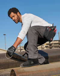 A worker wears the STRAUSS Performance Long Sleeve Shirt in white with tan work pants beside jobsite equipment