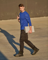 A worker wears the STRAUSS Performance Long Sleeve Shirt in royal blue with tan work pants beside jobsite equipment