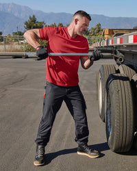 A worker wears the STRAUSS Performance T-Shirt in fire red with tan work pants while working in a field