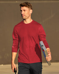 A worker wears the STRAUSS Performance Long Sleeve Shirt in fire red with tan work pants beside jobsite equipment
