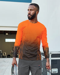 A worker wears the STRAUSS Enhanced Visibility Performance Long Sleeve Shirt e.s.t:aktik in neon orange and black with black work pants beside construction fencing
