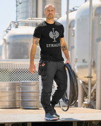 A model wears the STRAUSS T-Shirt e.s.concrete in black with matching work pants in a monochrome workwear outfit