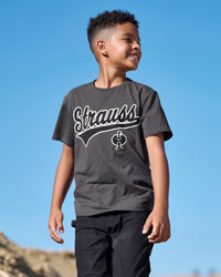 A child wears the Kids' STRAUSS Artwork T-Shirt e.s.e:pic in carbon gray under a clear blue sky