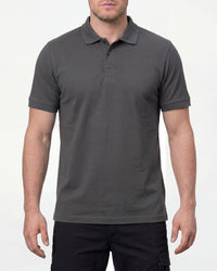 A model wears the STRAUSS Cotton Stretch Polo Shirt in carbon gray with tan work pants and work boots in a studio product scene
