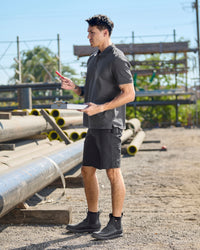 A worker wears the STRAUSS Cotton Stretch Polo Shirt in carbon gray with tan work pants while working