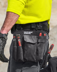 A worker wears a black STRAUSS e.s.tool concept left-hand large tool bag on a tool belt with utility work pants.