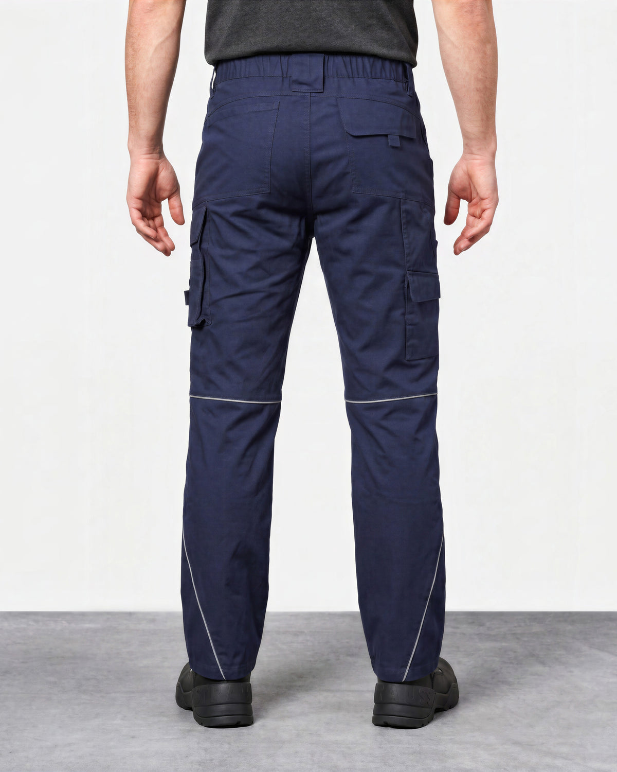 Rear view of a person wearing navy cargo work pants with white contrast stitching, shown against a plain light gray studio background.