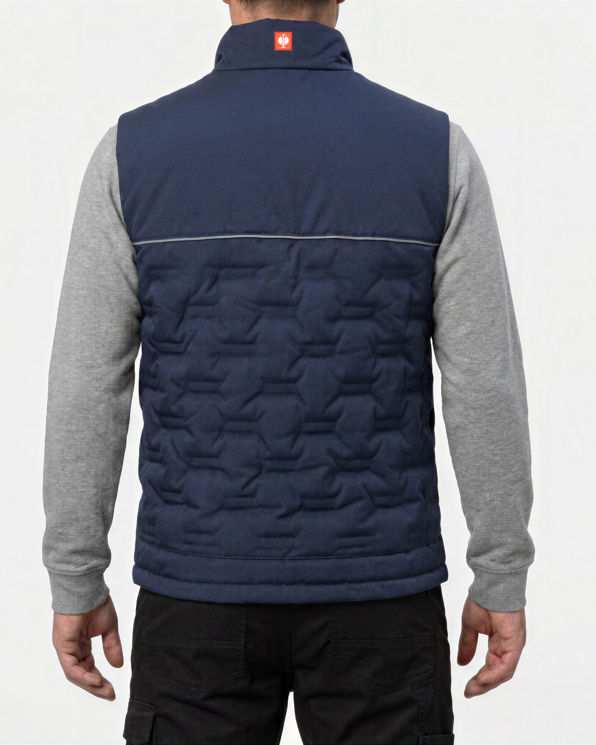 A man viewed from the back wearing a navy blue quilted vest over a gray long-sleeve shirt and black pants, against a plain light background.