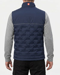 A man viewed from the back wearing a navy blue quilted vest over a gray long-sleeve shirt and black pants, against a plain light background.
