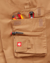 Close-up of a tan utility pocket on a matching tan garment, holding tools and a pen, with a small red STRAUSS logo patch on the pocket flap.