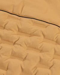 Close-up of a quilted fabric surface in a warm camel tan color with a thin black piping detail running horizontally.