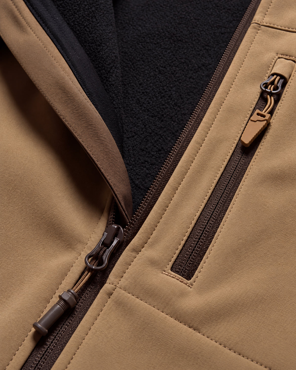 Close-up of a tan fleece-lined zippered jacket showing the tan exterior fabric, dark brown zipper trim, and a black fleece interior.