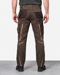 Rear view of a person wearing brown work pants with tan contrast zippers and pocket details, standing against a light gray studio background.