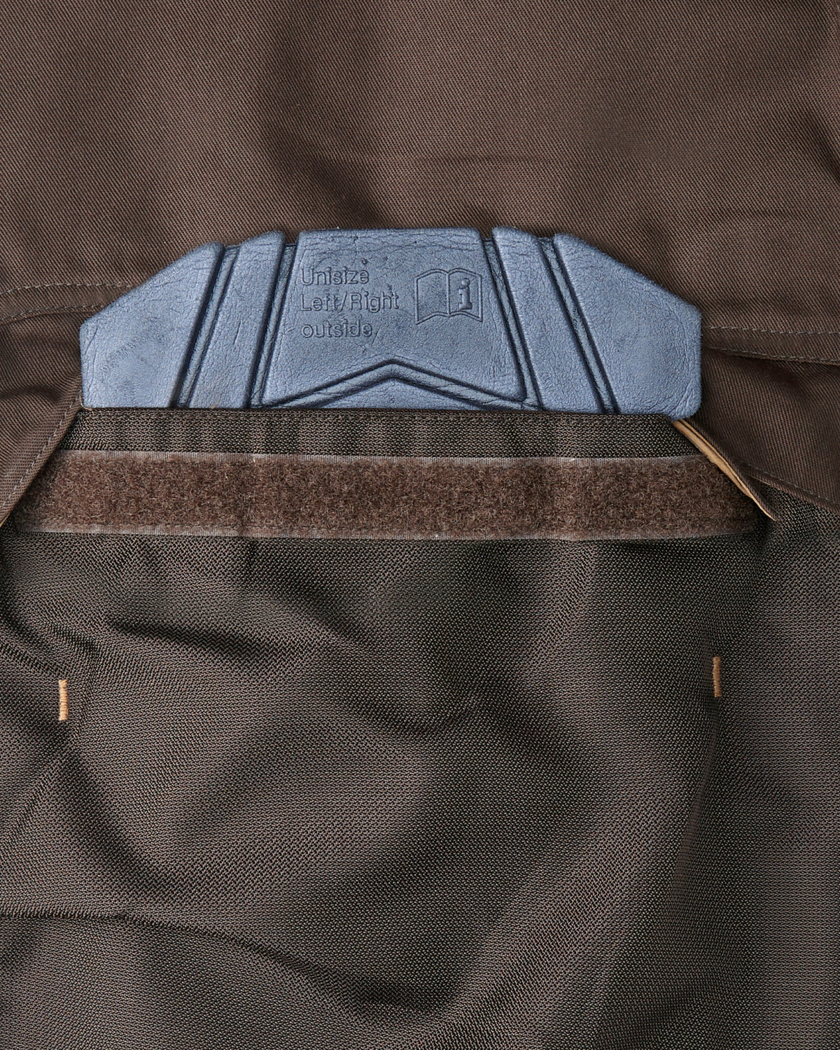 Close-up of a brown knee pad pocket showing a knee pad being inserted.