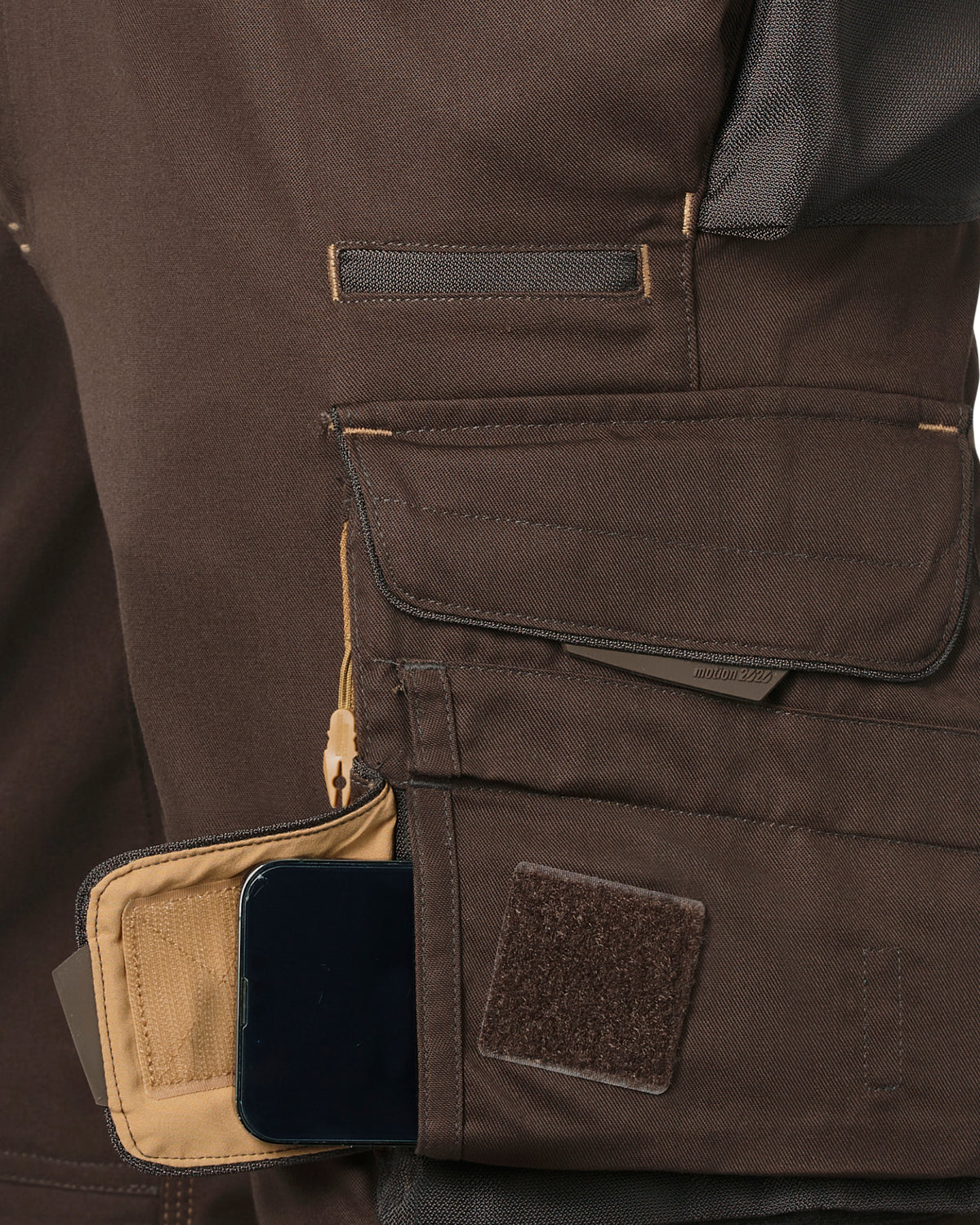 Close-up of brown tactical shorts with multiple utility pockets, including a tan interior pocket holding a black smartphone and a hook-and-loop patch.