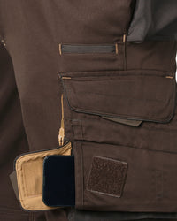 Close-up of brown tactical shorts with multiple utility pockets, including a tan interior pocket holding a black smartphone and a hook-and-loop patch.