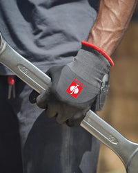 A worker wears black and gray STRAUSS evertouch winter nitrile foam gloves while gripping a hand tool at a workbench.