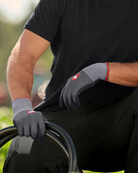 A worker wears black and gray STRAUSS evertouch micro nitrile foam gloves while gripping a hand tool at a workbench.