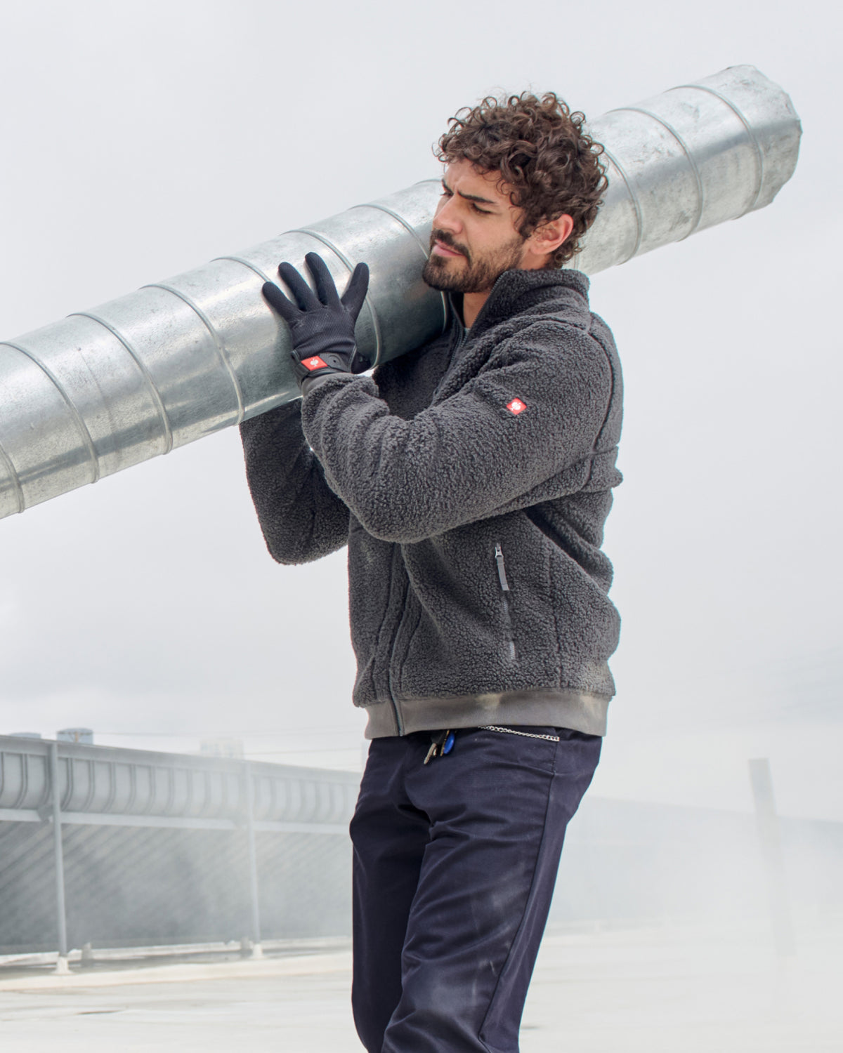 A worker wears black STRAUSS light assembly protection gloves while carrying materials.
