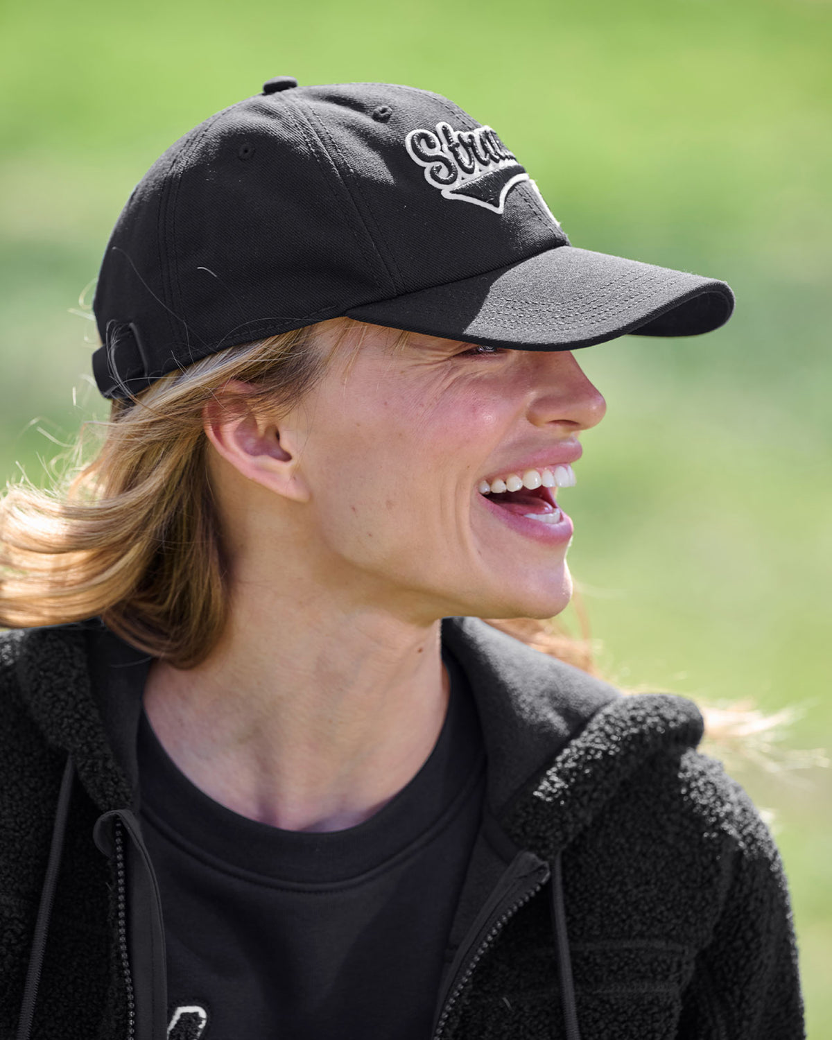 A worker wears a black STRAUSS e.s.e:pic cap with a work shirt and utility pants outdoors.