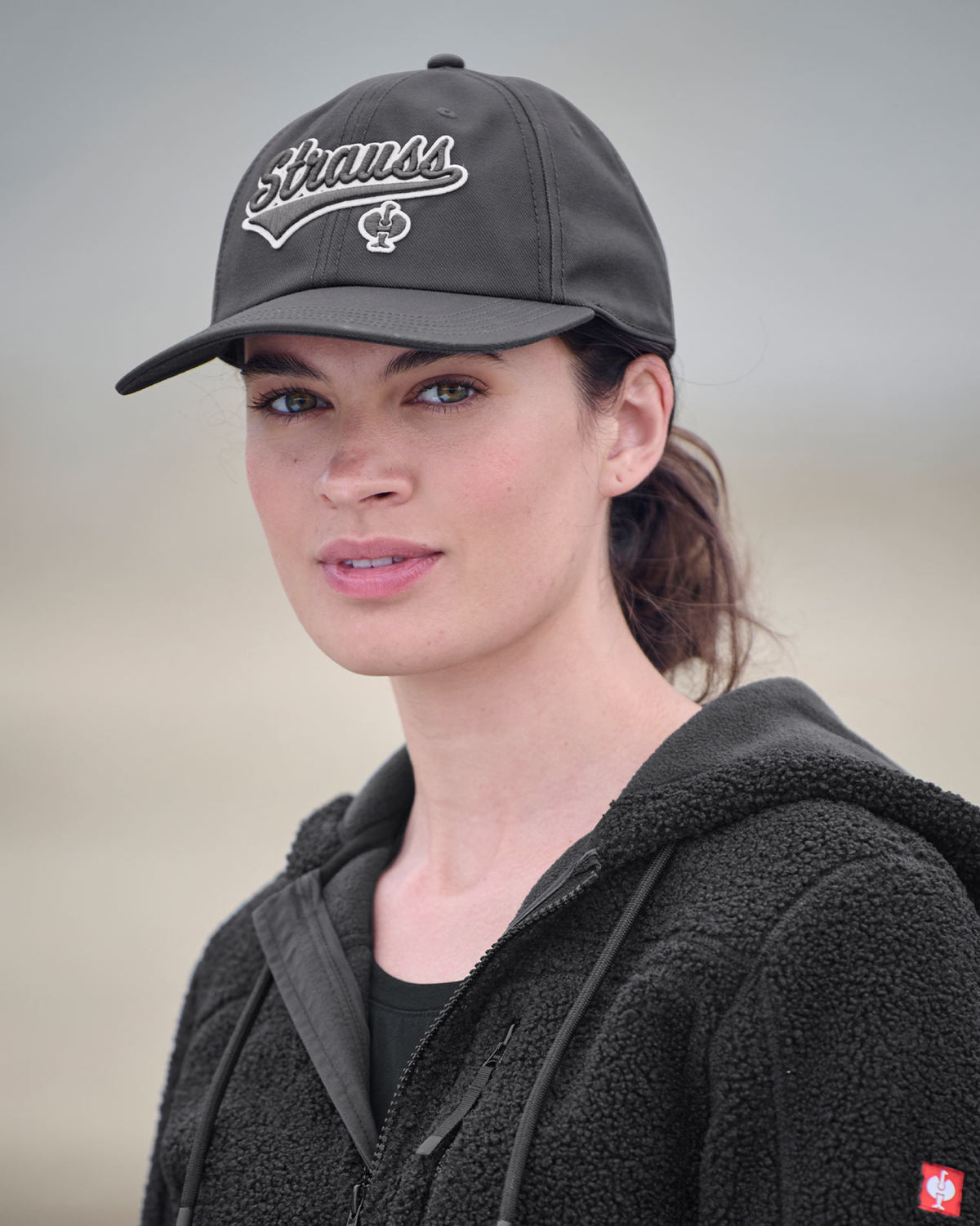 A worker in a carbon gray STRAUSS e.s.e:pic cap stands near jobsite materials in outdoor workwear.