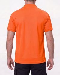 A model wears the STRAUSS Enhanced Visibility Performance Polo Shirt in neon orange with dark work pants and work boots, showing the shirt fit