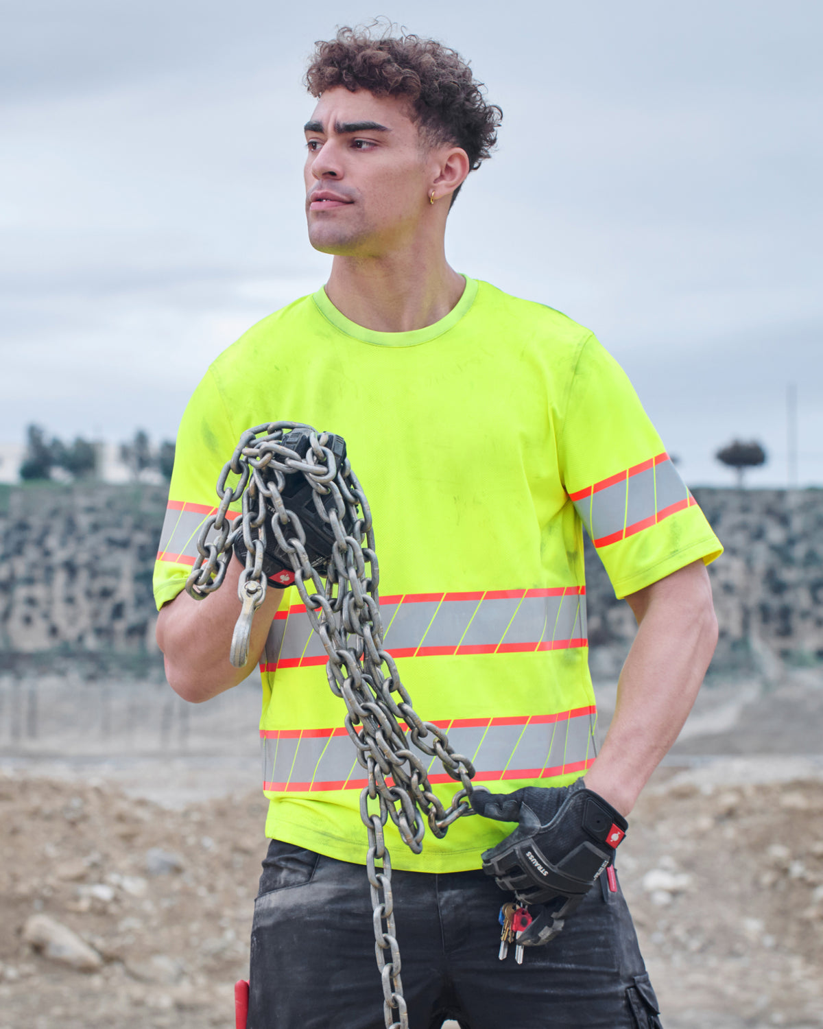 A worker wears the STRAUSS Class 2 High Visibility T-Shirt in neon yellow with dark work pants near construction equipment