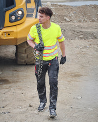 A worker wears the STRAUSS Class 2 High Visibility T-Shirt in neon yellow with work pants while handling materials at a jobsite