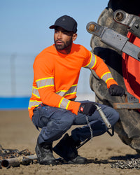 A worker wears the STRAUSS Class 2 High Visibility Long Sleeve Shirt in neon orange with work pants while handling materials at a jobsite