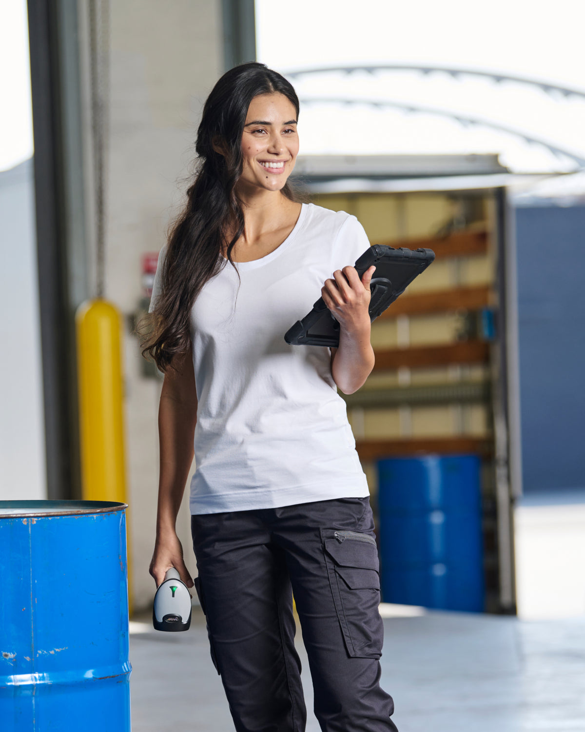 A woman wears the Women's STRAUSS Cotton Stretch T-Shirt in white with work pants in a workshop scene