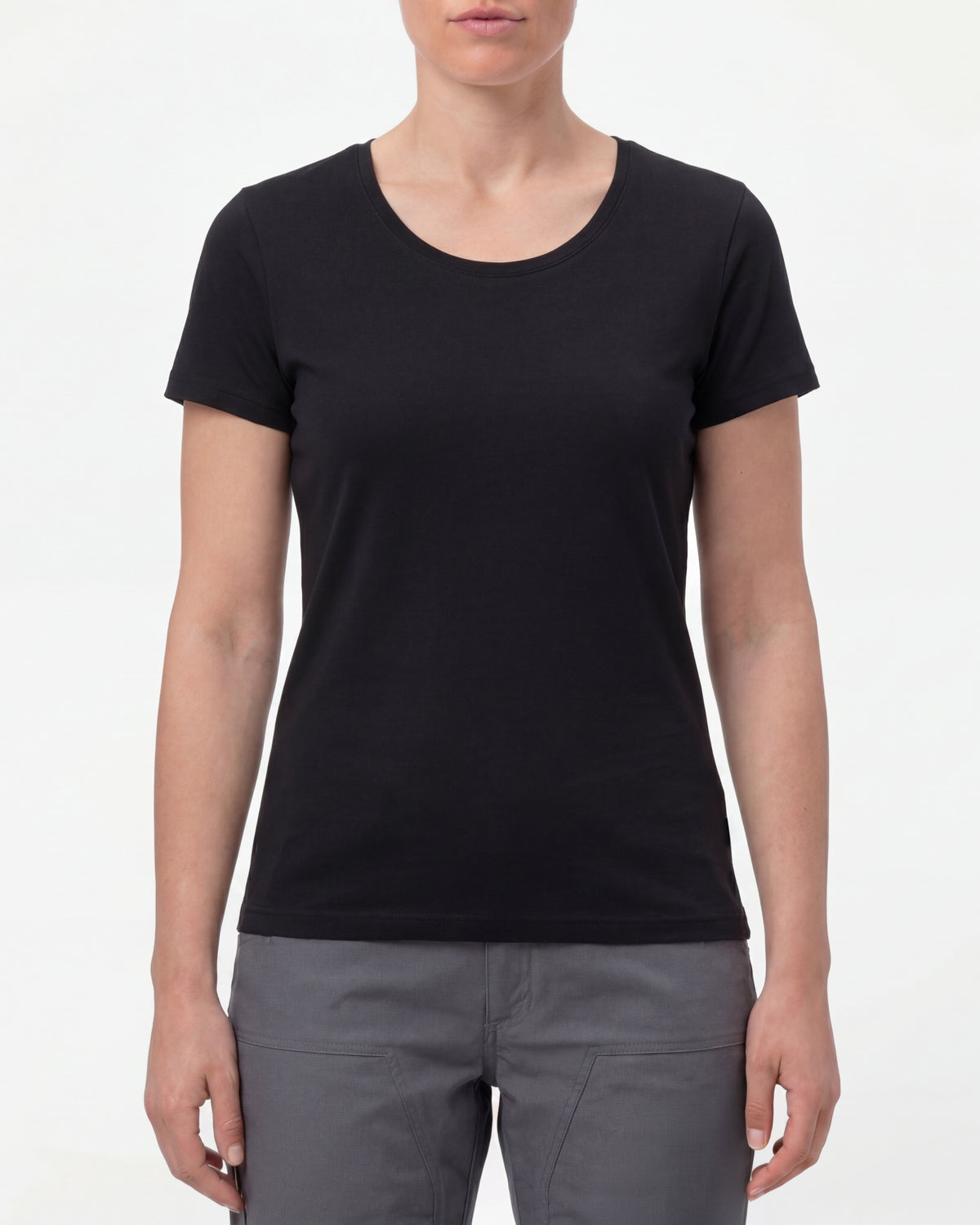 A woman wears the Women's STRAUSS Cotton Stretch T-Shirt in black with work pants and work boots in a studio product scene