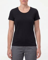 A woman wears the Women's STRAUSS Cotton Stretch T-Shirt in black with work pants and work boots in a studio product scene