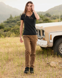 A woman wears the Women's STRAUSS Cotton Stretch T-Shirt in black with work pants beside a field
