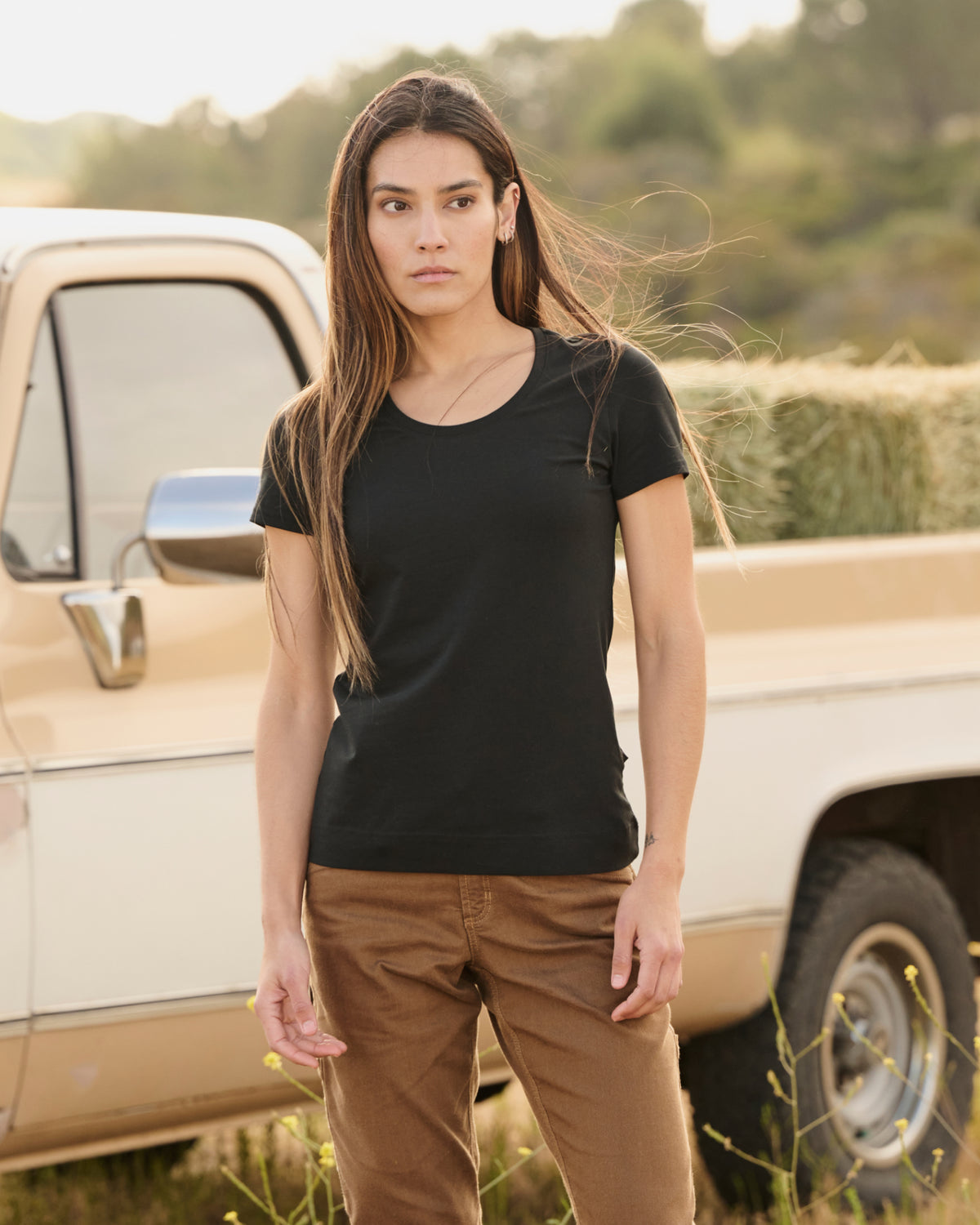 A woman wears the Women's STRAUSS Cotton Stretch T-Shirt in black with work pants on a sunny outdoor workday