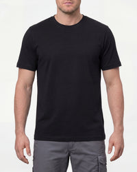 A model wears the STRAUSS Cotton T-Shirt in black with tan work pants and work boots in a studio product scene