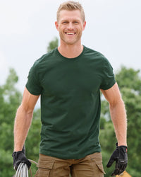 A worker wears the STRAUSS Cotton T-Shirt in green with tan work pants on a sunny jobsite