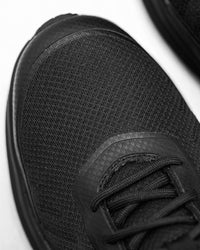Close-up of a black athletic shoe showing the textured mesh upper, laces, and a portion of the sole on a white background.