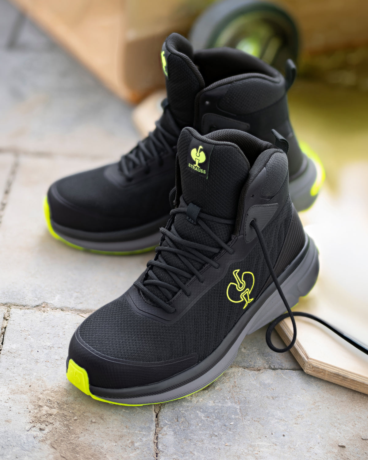 A pair of black high-top athletic boots with bright neon yellow-green accents on the soles and tongue logo, displayed on a stone surface.