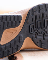 Close-up of the outsole of a sneaker, showing a black treaded rubber bottom with a tan and beige midsole section.