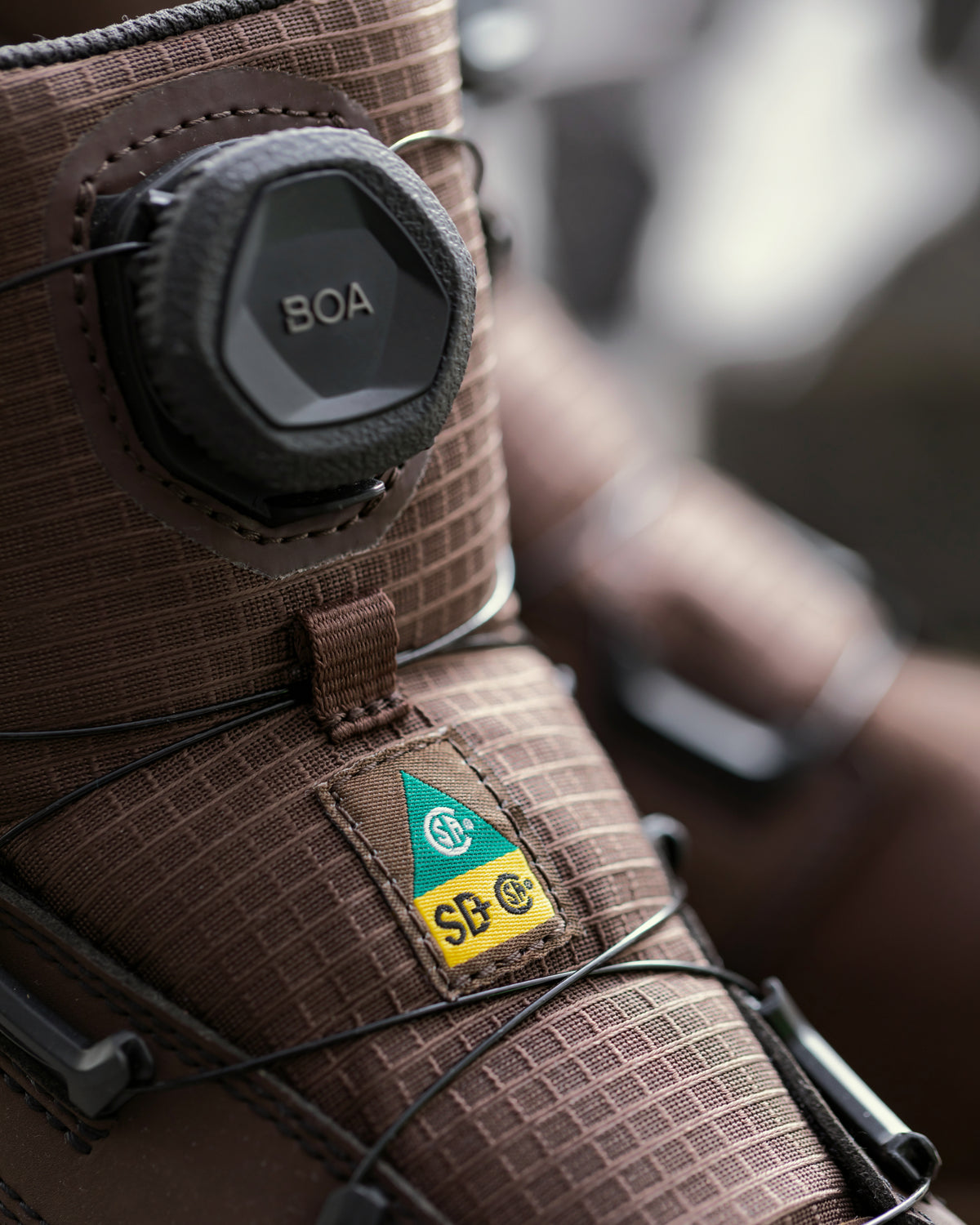 Close-up of a brown textured snowboard boot featuring a BOA dial closure and an SB C. G. brand patch.