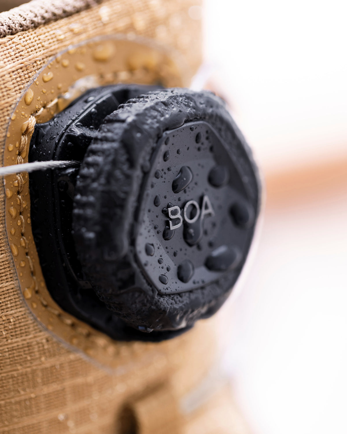 Close-up of a black waterproof cap with 'BOA' printed on it, attached to a tan fabric device covered in water droplets.