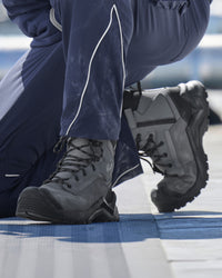 A close-up of a person wearing dark gray and black high-top work boots with navy blue pants, kneeling on a blue and white surface.