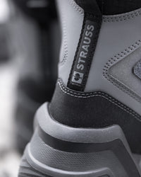 Close-up of a gray and black boot with a black pull tab displaying the brand name 'STRAUSS'.