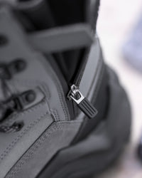 Close-up detail of a dark gray tactical boot showing the side zipper with a black pull tab and metal slider.
