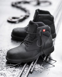 A pair of black high-top work boots arranged on a metallic surface with rebar and small metal shavings. One boot is in sharp focus in the foreground, while the second is slightly blurred behind it.